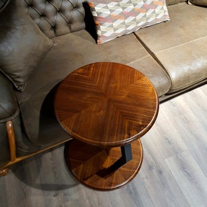 May include: A round wooden side table with a black metal base. The table has a dark brown wood finish and a chevron pattern on the top.