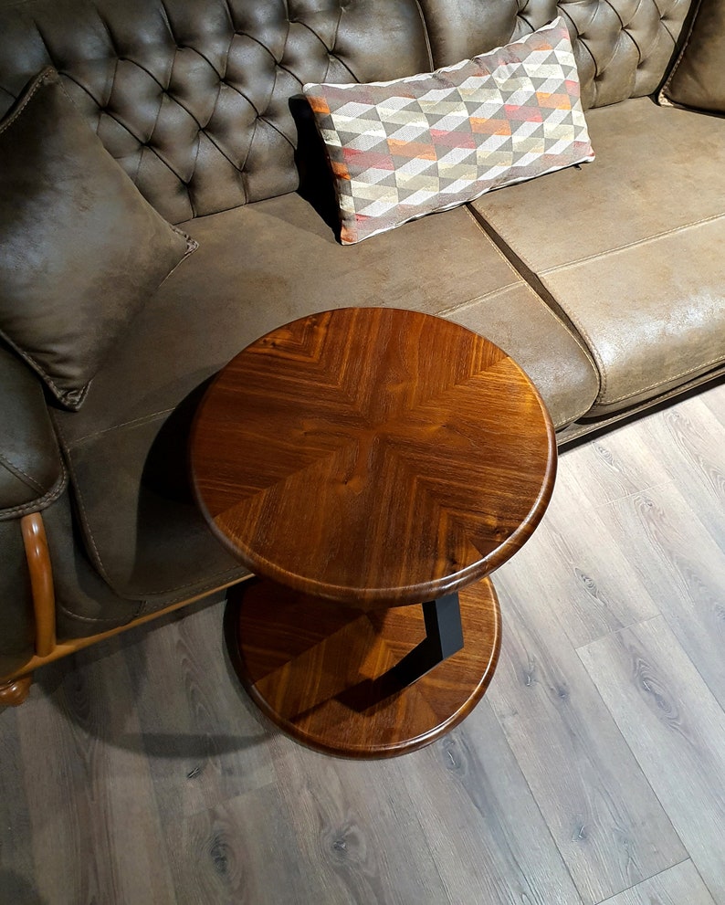 May include: A round wooden side table with a black metal base. The table has a dark brown wood finish and a chevron pattern on the top.