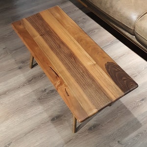 May include: A wooden coffee table with a natural wood finish and gold metal legs. The table top is made of multiple pieces of wood that have been joined together to create a unique pattern.