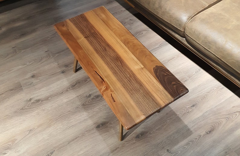 May include: A wooden coffee table with a natural wood finish and gold metal legs. The table top is made of multiple pieces of wood that have been joined together to create a unique pattern.