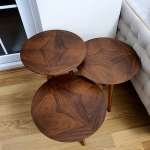 May include: A trio of round side tables with a distinctive design. Each table features a dark brown, patterned top and three slender legs. The tables are made of wood, with a starburst pattern on the surface, and are arranged in a cluster.
