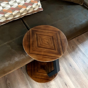 May include: A round wooden side table with a dark brown wood top and a black metal base. The table has a geometric pattern on the top.