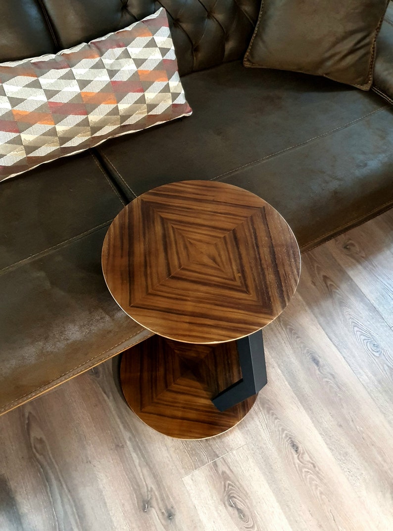 May include: A round wooden side table with a dark brown wood top and a black metal base. The table has a geometric pattern on the top.
