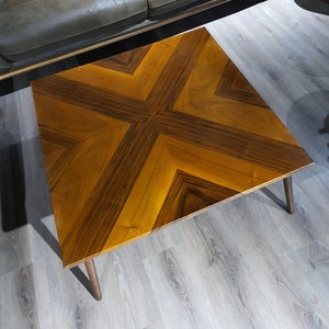 May include: A wooden coffee table with a geometric pattern in shades of brown. The table has a square top and four legs.