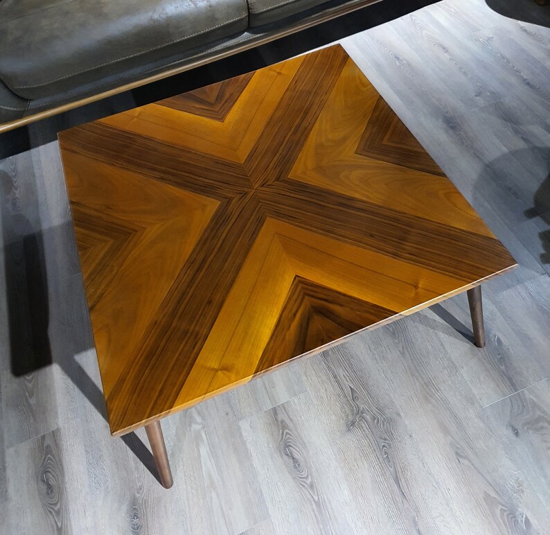 May include: A wooden coffee table with a geometric pattern in shades of brown. The table has a square top and four legs.