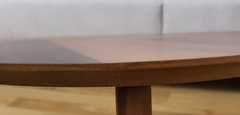 May include: A close-up of a round wooden table with a brown tabletop and a single leg. The tabletop has a two-tone design, with a darker brown section. The table is likely a piece of furniture.