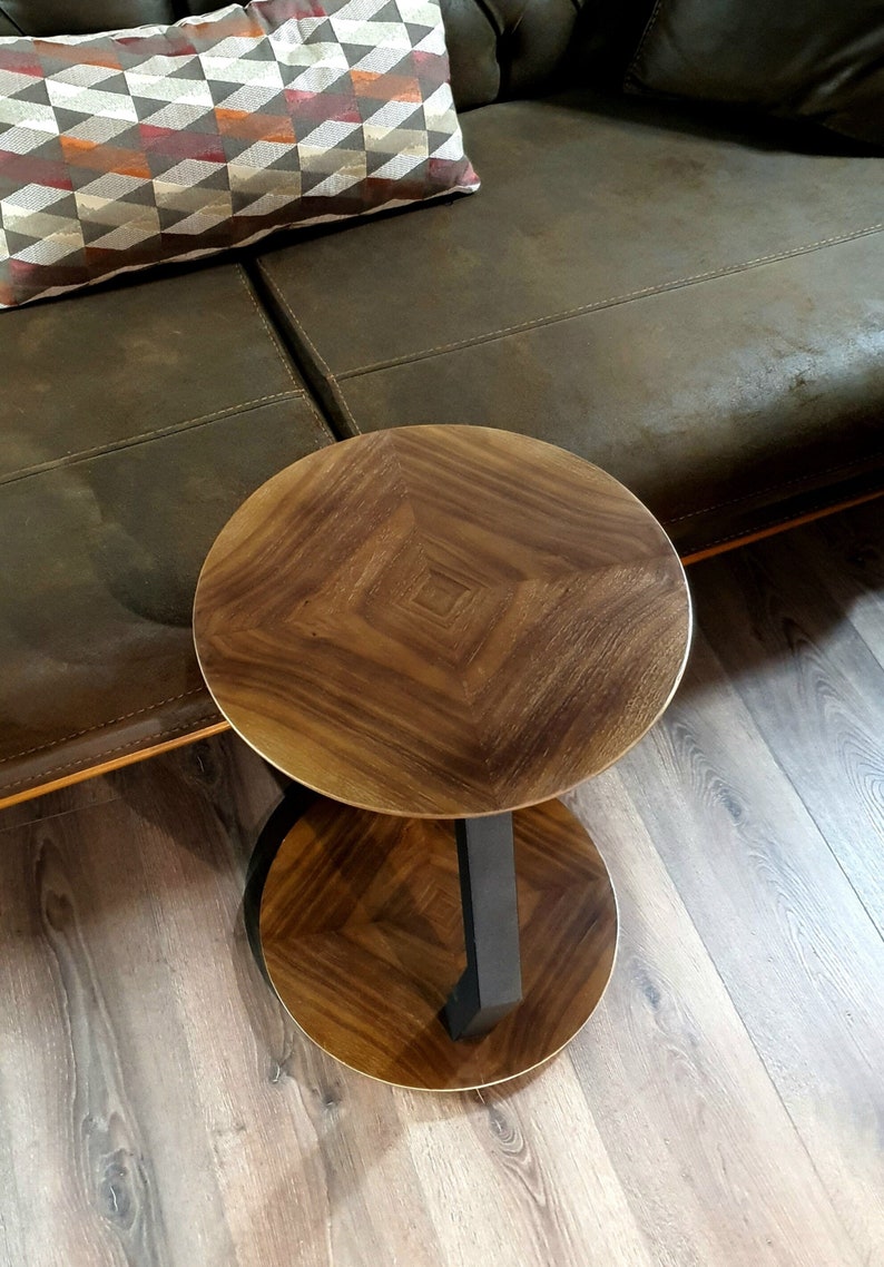 May include: A round wooden side table with a dark brown wood top and a black metal base. The table has a unique design with a diamond pattern in the wood.