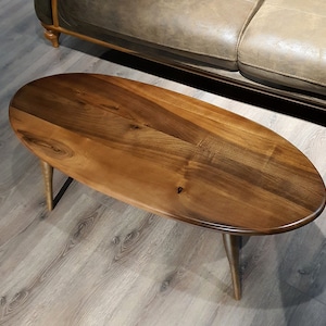 May include: A wooden oval coffee table with a dark brown stain. The table has a simple design with four legs.