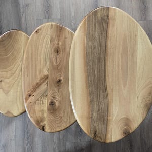 May include: Three wooden oval-shaped nesting tables with a natural wood grain finish. The tables are arranged in size order, with the largest table at the top and the smallest table at the bottom.