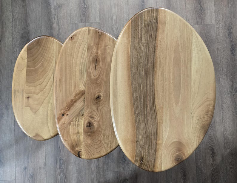 May include: Three wooden oval-shaped nesting tables with a natural wood grain finish. The tables are arranged in size order, with the largest table at the top and the smallest table at the bottom.