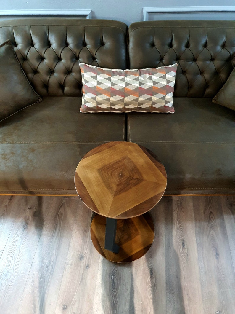May include: A brown leather sofa with a patterned pillow and a round wooden side table with a black metal base.
