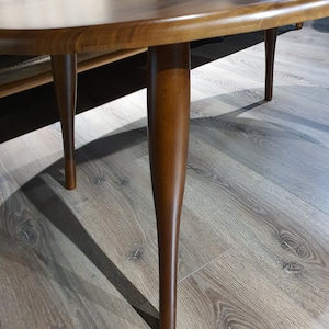 May include: A wooden oval coffee table with a dark brown finish and four slender legs.