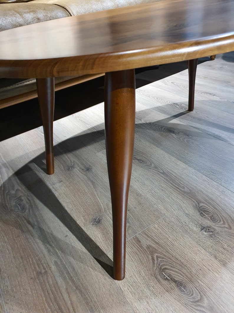May include: A wooden oval coffee table with a dark brown finish and four slender legs.