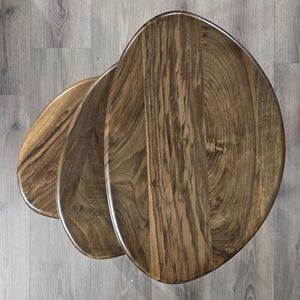 May include: A set of three wooden nesting tables with a unique organic shape. The tables are made of dark brown wood with a natural grain pattern.
