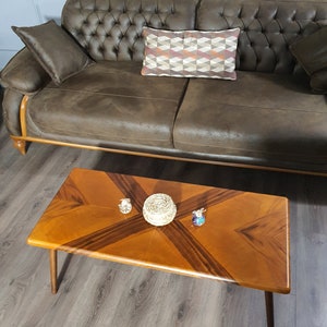 May include: A brown leather sofa with a tufted back and a rectangular coffee table. The coffee table has a light brown wood grain pattern with dark brown accents. Decorative items sit on the table, including a woven basket and small glass figurines.