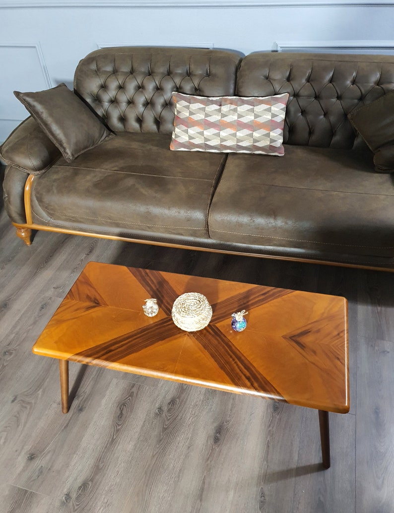 May include: A brown leather sofa with a tufted back and a rectangular coffee table. The coffee table has a light brown wood grain pattern with dark brown accents. Decorative items sit on the table, including a woven basket and small glass figurines.
