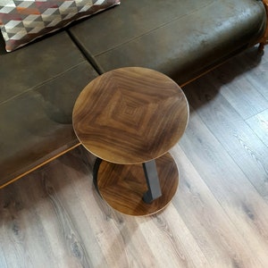 May include: A two-tiered wooden side table with a dark brown wood finish and a black metal base. The table has a round top and a lower shelf.