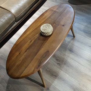 May include: A dark brown oval-shaped wooden coffee table with a woven coaster on top. The table has four legs and is sitting on a light brown wood floor.
