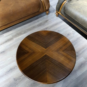 May include: A round wooden coffee table with a dark brown wood grain pattern. The table top has a geometric design with a cross shape in the center.