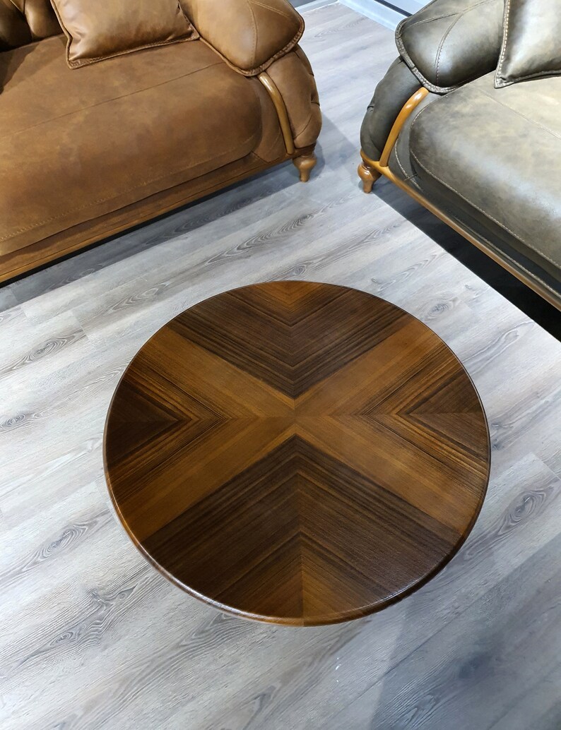 May include: A round wooden coffee table with a dark brown wood grain pattern. The table top has a geometric design with a cross shape in the center.