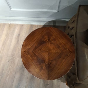 May include: A round wooden table top with a dark brown wood grain pattern. The table top has a geometric design with a diamond shape in the center.