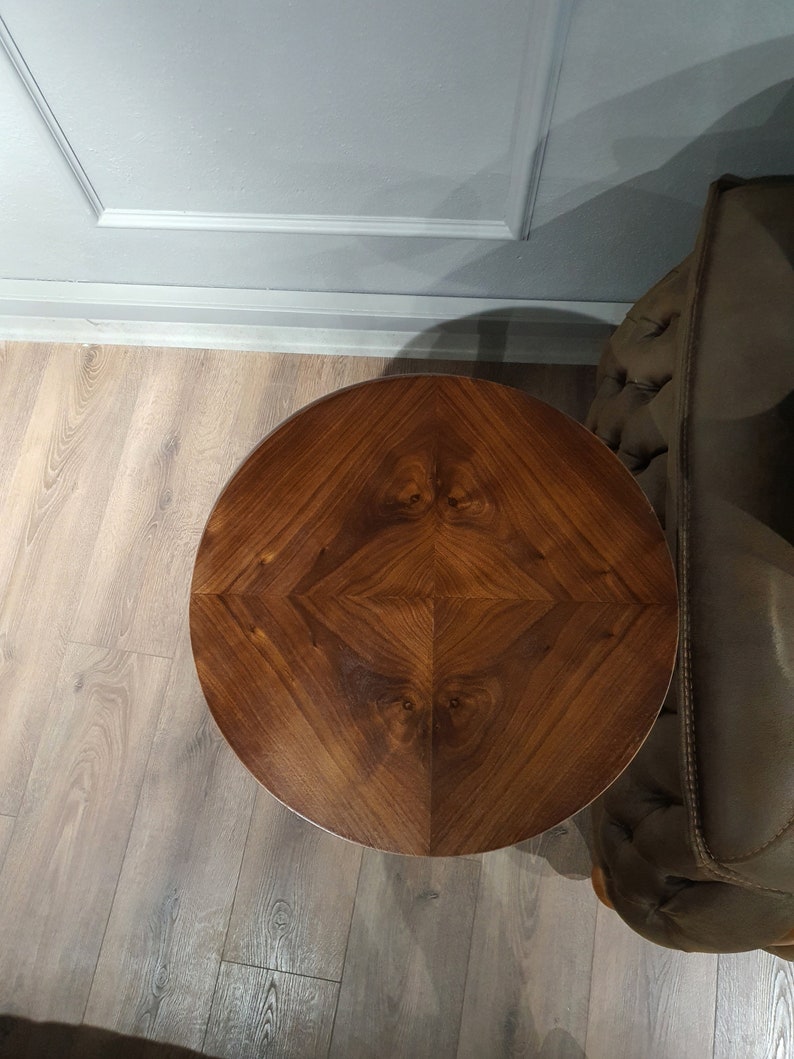 May include: A round wooden table top with a dark brown wood grain pattern. The table top has a geometric design with a diamond shape in the center.
