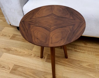 May include: A round wooden side table with a dark brown wood grain finish and three legs. The table is sitting on a light wood floor.