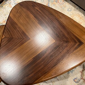 May include: Two wooden, triangular-shaped side tables with a chevron pattern. The tables are made of dark brown and light brown wood, with a glossy finish. The tables are likely used for home decor.