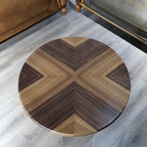 May include: A round wooden coffee table with a dark brown and light brown wood grain pattern. The table top has a geometric design with a cross shape in the center.