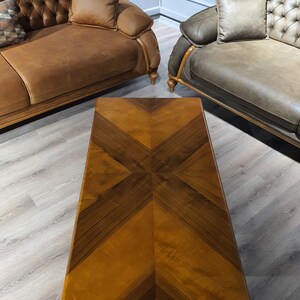 May include: A rectangular wooden coffee table with a brown wood top featuring a geometric pattern of inlaid wood. The table is sitting on a light wood floor.
