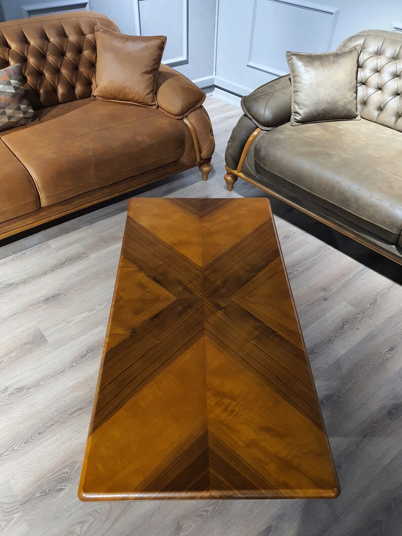 May include: A rectangular wooden coffee table with a brown wood top featuring a geometric pattern of inlaid wood. The table is sitting on a light wood floor.