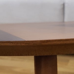 K&ouml;nnte beinhalten: Nahaufnahme der Kante eines runden Holztisches mit hellbrauner Oberfl&auml;che. Der Tisch hat ein einzelnes Bein, das in der unteren rechten Ecke sichtbar ist.