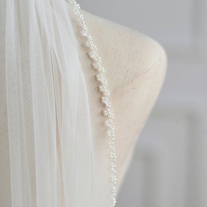 May include: A white bridal veil with a beaded edge. The veil is made of soft tulle and has a delicate, romantic look.