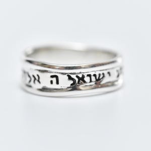 Può includere: Un anello d'argento con scrittura ebraica incisa attorno alla fascia.