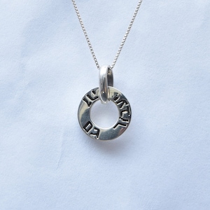 May include: Silver necklace with a round pendant inscribed with Hebrew text. The pendant is a circle with a smaller circle in the center. The text on the pendant is in Hebrew.
