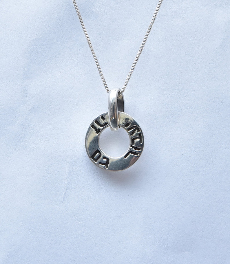 May include: Silver necklace with a round pendant inscribed with Hebrew text. The pendant is a circle with a smaller circle in the center. The text on the pendant is in Hebrew.