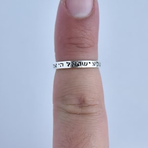 Op de afbeelding: Een zilveren ring met Hebreeuwse tekst erop gegraveerd. De ring wordt aan een vinger gedragen.