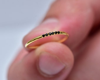 May include: A thin gold band ring with a row of small black gemstones.