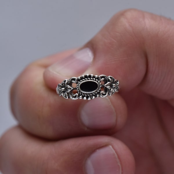 May include: A silver ring with a black oval stone and floral details.