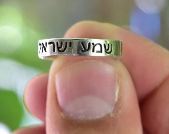 Könnte beinhalten: Ein silberner Ring mit den hebräischen Worten "Shabbat Shalom" eingraviert.