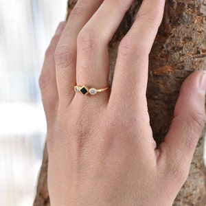 May include: Gold ring with three square-shaped stones. The center stone is black, and the stones on either side are clear.