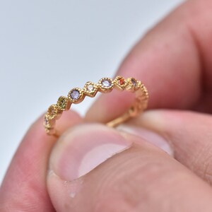 Può includere: Un anello a fascia d'oro con una fila di pietre preziose colorate. Le pietre preziose sono incastonate in un design a festoni.