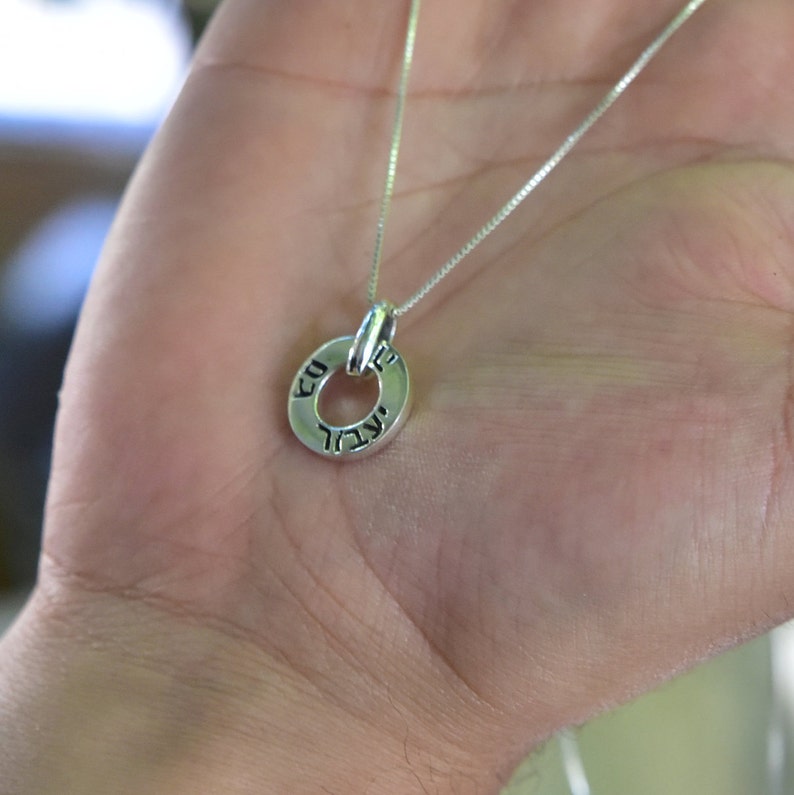 May include: A silver chain necklace with a small silver circle pendant. The pendant has Hebrew writing around the edge.