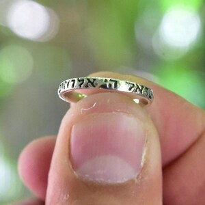 Puede incluir: Un anillo de plata con letras hebreas inscritas alrededor de la banda. Las letras dicen "אמת ואהבה" que se traduce como "Verdad y Amor".