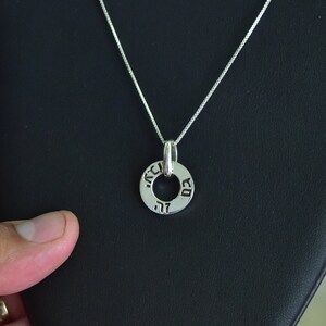 May include: A silver chain necklace with a silver pendant. The pendant is a circle with Hebrew writing around the edge.