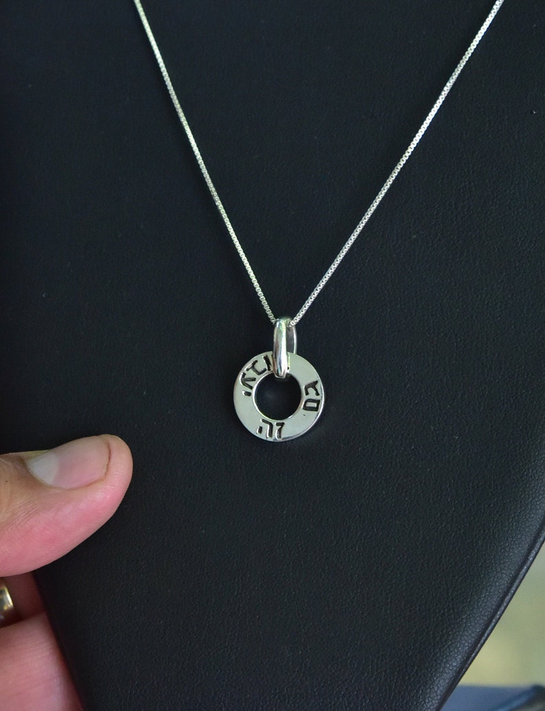 May include: A silver chain necklace with a silver pendant. The pendant is a circle with Hebrew writing around the edge.