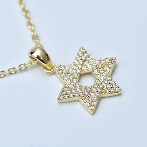 May include: A gold chain necklace with a pendant in the shape of a Star of David. The pendant is covered in small, clear cubic zirconia stones.