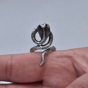 May include: A silver ring featuring a detailed cobra snake design. The snake is coiled with its head raised and its hood expanded.