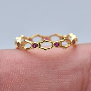 May include: A gold band ring with a delicate, intricate design featuring small pink gemstones.