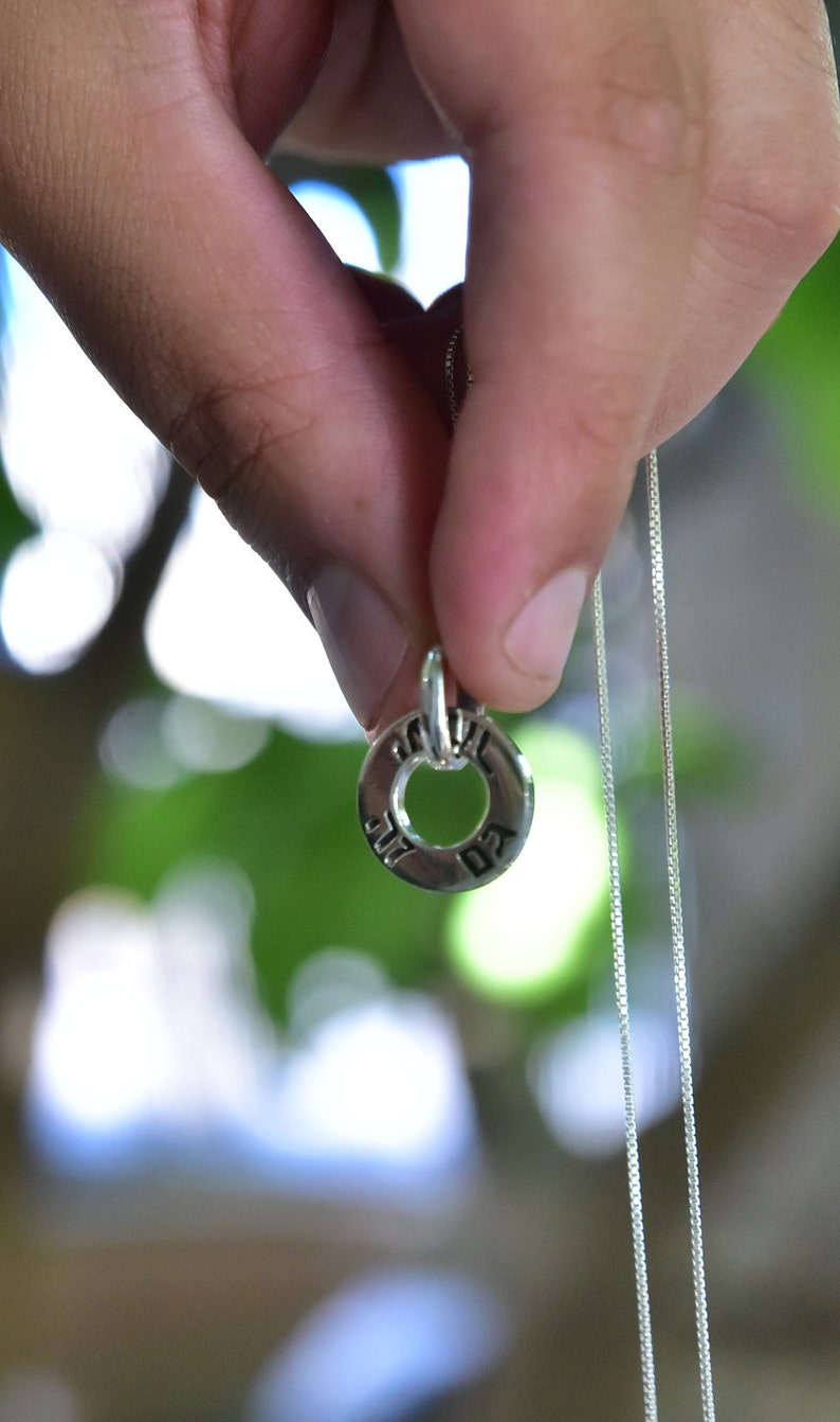 May include: A silver chain necklace with a round pendant featuring Hebrew lettering.